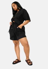 Haut court en lin noir à manches courtes associé à un short assorti. Sandales marron avec clous et détail de nœud. Tenue simple et décontractée.