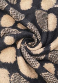 Tessuto a maglia nero e beige con motivo, caratterizzato da grandi macchie pelose e un design testurizzato con una consistenza morbida simile alla lana.