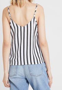 Top a spaghetto a righe bianche e nere, caratterizzato da strisce verticali. Materiale leggero con una vestibilità rilassata. Indossato con jeans blu.