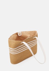 Slámová taška na tote s bílými vodorovnými pruhy, obdélníkový tvar, dvojité bílé držadla a béžové textilní podšívka. Knoflíkové zapínání na vrchu.
