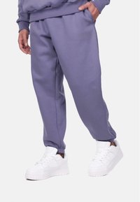 Purple sweatpants made of cotton blend with a relaxed fit, featuring an elastic waistband and cuffs, paired with white sneakers.