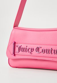 Rózsaszín műbőr kézitáska, dombornyomott "Juicy Couture" logóval, ellentétes fényes hardverrel és sima, textúrázott felülettel.