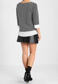 Svartvitt mönstrad topp med trekvartsärmar, lager på lager över en vit blus; matchad med en svart läderskjol och ankelstövlar.