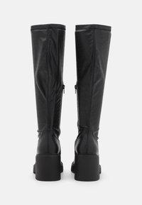 Bottes noires montant jusqu'aux genoux avec talons carrés, fermetures éclair à l'arrière et matériau lisse, vues de dos sur fond blanc.