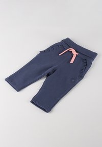 Navyblaue Sweatpants aus weichem Stoff, mit einem pinkfarbenen Kordelzug, gerüschten Seitenelementen und einem gestickten Logo am Bein.