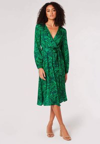 Robes vertes nouées avec un motif ondulé, manches longues et lien à la taille. Longueur midi, fabriquée dans un tissu lisse. Design décontracté.