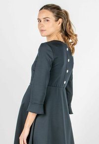 Ein dunkelgraues, langärmliges Kleid mit einem taillierten Oberteil und einem ausgestellten Rock, das mit Knopfdetails auf dem Rücken und glockenförmigen Ärmelbündchen versehen ist.
