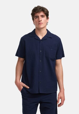 Marineblauw overhemd met korte mouwen, voorzien van een textuurpatroon, knoopsluiting aan de voorkant en een borstzak aan de linkerkant. Gemaakt van ademende stof.