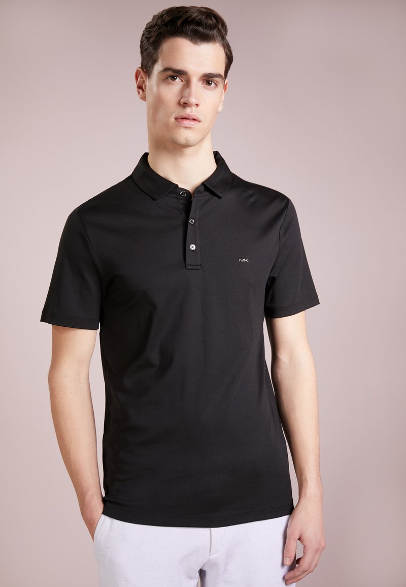 Svart polo skjorte laget av myk bomull. Har en klassisk krage, tre knapper i placket, og en liten logo på venstre bryst. Korte ermer.
