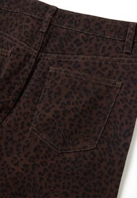 Tessuto in corduroy marrone con un motivo a stampa leopardata. Presenta una tasca posteriore con dettagli di cucitura visibili. La superficie testurizzata aggiunge profondità.