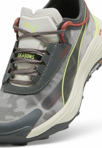 Baskets de sport grises avec une tige en textile à motifs, des lignes d'accent jaune fluo, des éléments en rouge et une semelle texturée pour l'adhérence.