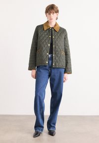 Gequiltede groene jas met een beige kraag en gouden drukknoopjes, gecombineerd met wijde blauwe spijkerbroek en puntige zwarte schoenen.