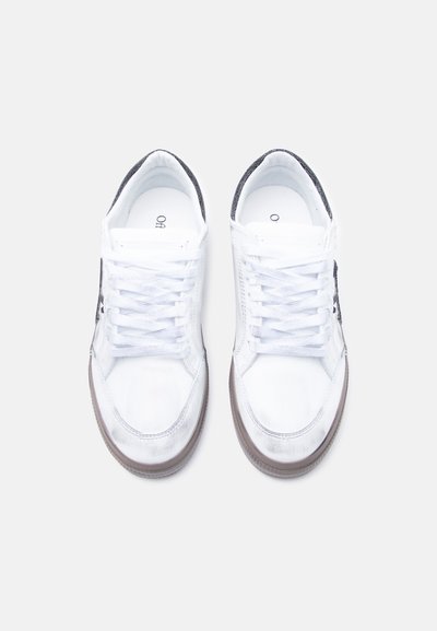 Baskets en cuir blanc au design simple, bout rond et accents en tissu gris. Comprend des lacets blancs et une semelle en caoutchouc marron.