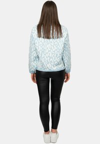 Maglione lavorato a maglia di un blu chiaro con stampa leopardo bianca, abbinato a leggins in pelle nera e sneakers bianche. Texture liscia e vestibilità rilassata.