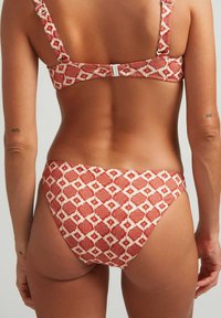 Parte superior e inferior de bikini con un diseño rojo y patrones geométricos blancos, tirantes ajustables y cierre de gancho en la parte posterior. Tela texturizada.