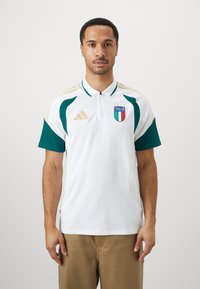 Hvit polo-skjorte med grønne sidelinjer, glidelåskrage og "ITALIA"-emblem. Gullstriper på skuldrene, laget av et pustende materiale.