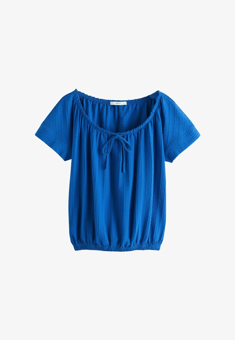 Niebieska bluzka z krótkim rękawem wykonana z fakturowanej tkaniny, z elastycznym dołem i dekoltem oraz małą kokardką na środku przodu.
