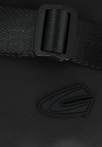 Schwarze Tasche mit einer strukturierten Nylonoberfläche, einem gewebten Gurt mit einer Kunststoffschnalle und einem auffälligen Gummi-Logo-Accessoire.