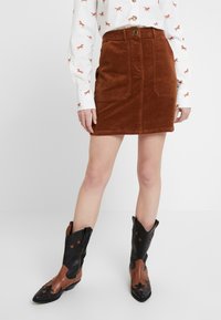 Minigonna in velluto a coste marrone con tasche frontali, abbinata a stivali da cowboy neri e marroni con accenti a forma di stella. Camicia bianca con motivo di cavalli.