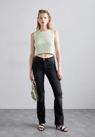 Light green ribbed crop top, high-waisted black flared jeans, black strappy sandals, and a small green bag with fringe detail.