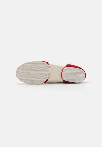 Rote und weiße Schuhe mit einer strukturierten Gummisohle, die ein Fischgrätenmuster aufweist, glatten Seiten und einem runden Zehendesign.