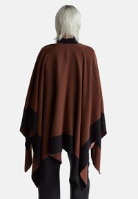 Hnědý a černý vzorovaný pončo s pleteným límcem, má tekoucí tříúhelníkový tvar a měkkou texturu.