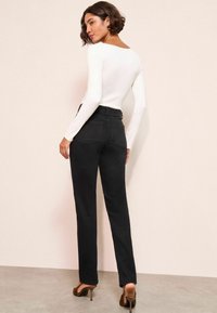 Jeans neri a vita alta con gamba diritta, dotati di tasche posteriori e texture liscia, abbinati a un top attillato a maniche lunghe bianco.