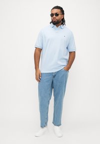 Lyseblå polo-shirt med korte ærmer, med et lille logo på brystet, kombineret med løstsiddende lyseblå jeans og hvide sneakers.