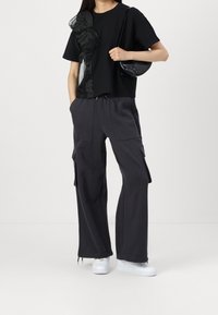 Černý top s krátkým rukávem s průhlednými detaily, v kombinaci s tmavě šedými kalhotami typu cargo s bočními kapsami a bílými teniskami. Součástí je černá kabelka.