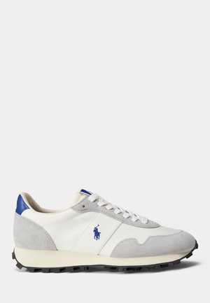 Sneaker bianca e grigia realizzata in materiali scamosciati e mesh, con un accento blu sul tallone e una suola in gomma grigia. Logo visibile sul lato.