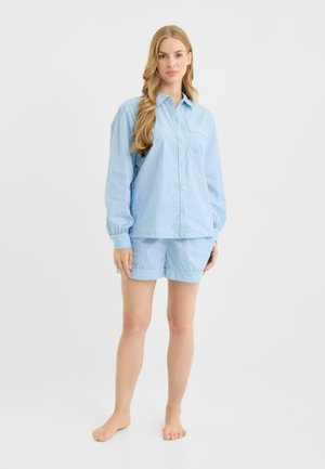 Lyseblåt ternet pyjamassæt bestående af en langærmet skjorte med knapper og matchende shorts. Grøn kant pryder ærmerne og shortsene.