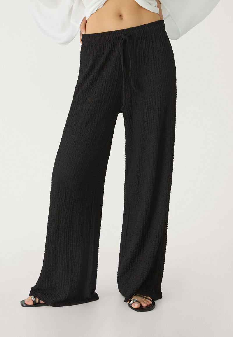 Schwarze, strukturierte, weite Hosen mit elastischem Bund und Kordelzug. Lockere Passform, leichtes Material und weicher, zerknitterter Look.