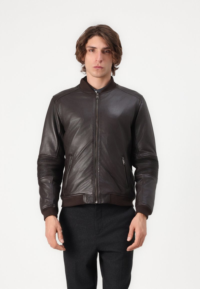 Bruine leren bomberjack met ritssluiting, geribde manchetten en zijzakken; heeft horizontale stiksels op de schouders voor textuur.