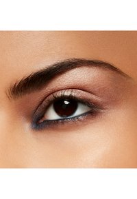 Nahaufnahme eines Auges mit einer dunkelbraunen Iris, schimmerndem, hellem Lidschatten und blauer Eyeliner. Glatte Hauttextur mit gut definiertem Augenbrauen.