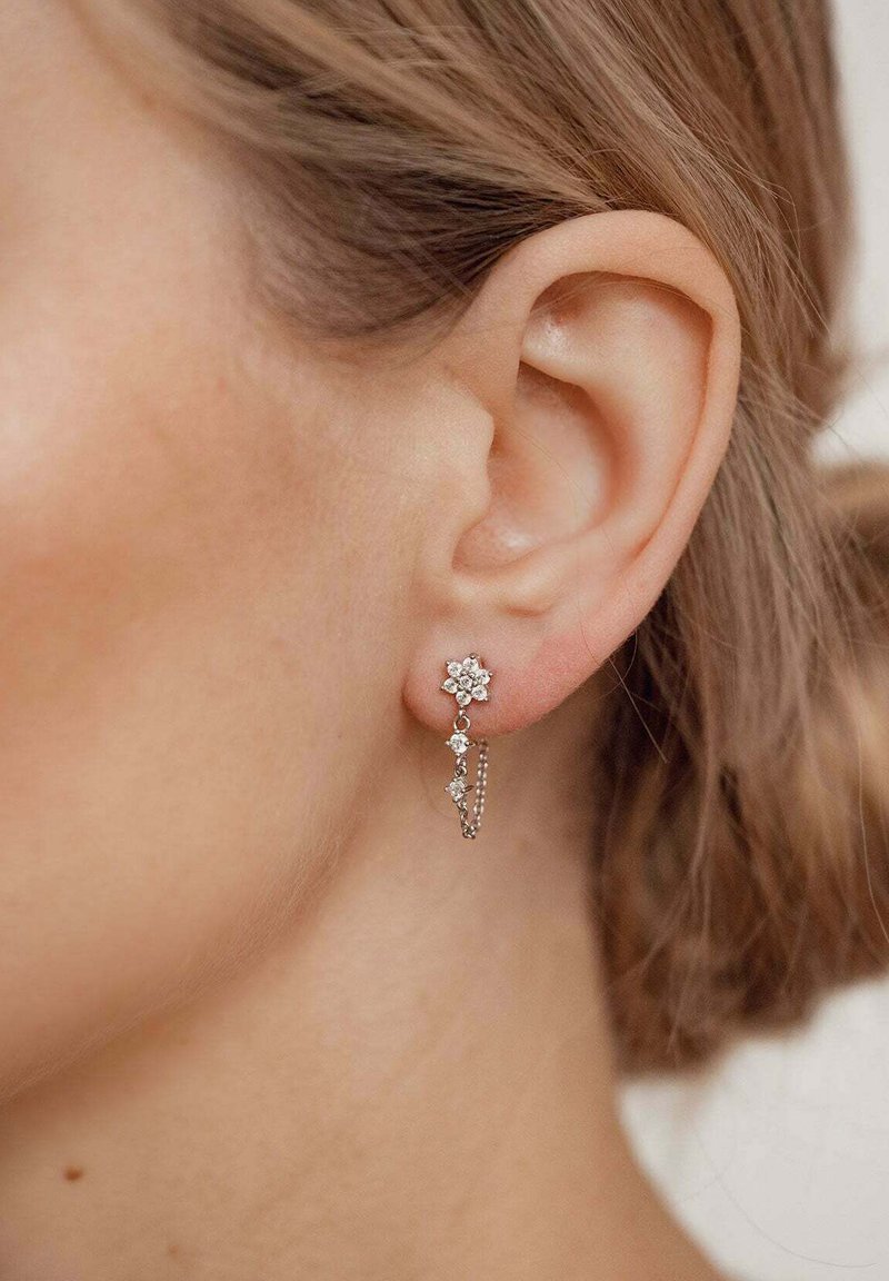 Silberne Tropfenohrringe mit floralem Design, verziert mit kleinen Edelsteinen, die zart an einem Kettenelement hängen.