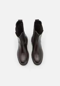 Botines negros de cuero brillante con paneles laterales elásticos. Tienen una puntera redondeada y una suela de goma texturizada para mayor agarre.