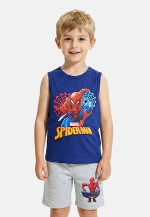 Jeune garçon debout, souriant, portant un débardeur bleu Spider-Man et un short gris avec un motif Spider-Man sur la jambe gauche.
