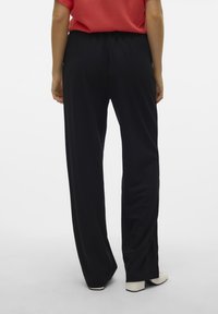 Pantaloni neri a gamba larga con fascia elastica in vita, caratterizzati da una texture morbida e una leggera caduta. Abbinati a scarpe con tacco beige.