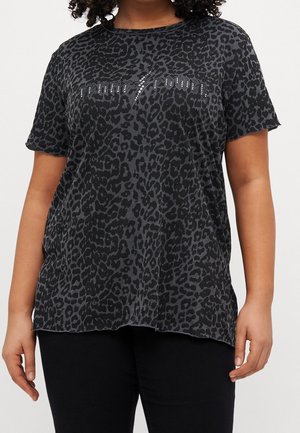 Frau trägt ein kurzärmeliges Shirt mit schwarzem und grauem Leopardenmuster und dem mit Nieten verzierten Schriftzug "Forever 1 young" über der Brust.