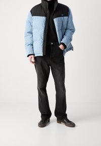 Pikowana kurtka w kolorze niebieskim i czarnym, z powtarzającym się nadrukiem "HUGO". Połączona z prostymi czarnymi dżinsami i ciemnymi butami. Prosty design.