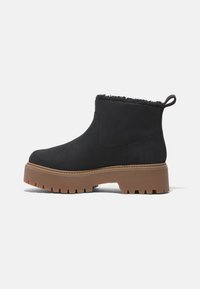 Black ankle boots with a soft, faux fur lining, sturdy rubber sole, and a chunky platform for added height and grip. Curved design with a pull tab.