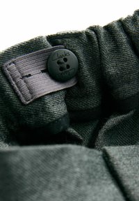 Sivi platneni pojas s elastičnom trakom i crnim dugmetom s ugraviranim natpisom "Clarks". Glatka tekstura s suptilnim detaljima šavova.