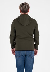 Felpa con cappuccio verde oliva, maniche lunghe, in misto cotone, vestibilità rilassata e tasca anteriore; abbinata a jeans in denim blu.