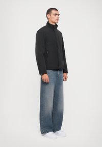 Svart, zip-up jacka med hög krage, som har sidofickor. Bärs med vida, urtvättade blå jeans och vita sneakers.