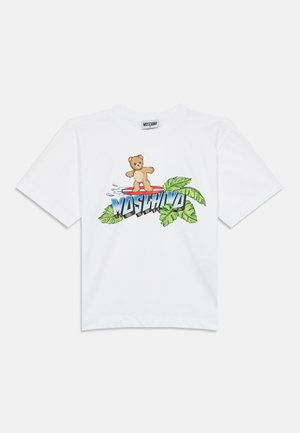 T-shirt bianca a maniche corte con un orso dei cartoni animati su una tavola da surf, con accenti di foglie tropicali e il testo audace "MOSCHINO" sotto il disegno.