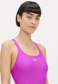 Traje de baño rosa brillante con tirantes finos y escote redondo. Presenta el logo de "arena" en azul claro en el pecho. Tejido liso y elástico.