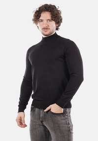 Maglione a collo alto nero dal design aderente, realizzato in un tessuto a maglia liscia, con maniche lunghe e orlo a costine. Accentuano la forma del corpo.