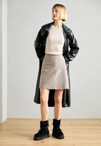 Fekete bőr trench kabát, bézs bordázott felső, bézs A-vonalú szoknya és fekete bunda bélelt bokacsizma. Minimalista dizájn és semleges árnyalatok.