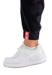 Weiße Nike Air Force 1 Sneaker mit Obermaterial aus strukturiertem Leder, Gummisohle und erhabenem "AIR"-Logo. Jogginghose aus schwarzem Velours mit rotem Akzent-Tag.