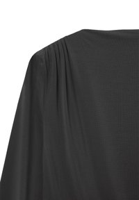 Tessuto nero con morbide pieghe vicino alla cucitura della spalla su un indumento a maniche lunghe, che mostra una consistenza e una caduta fluida.